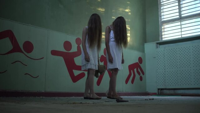Two girls stand in an abandoned high school gym holding hands, facial hair. Mother and daughter or two sisters. Horror.Abandoned house. Mysticism.