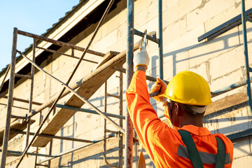 Naklejka na ściany i meble Construction worker wearing safety harness belt during working at high place,Concept of residential building under construction.