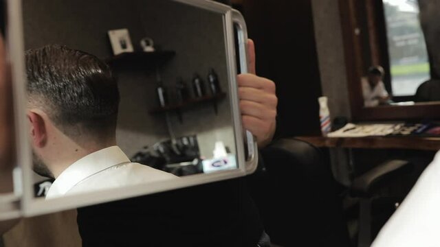 Attractive man is looking in the mirror after his haircut in barbershop. Happy client at the hair salon after haircut.