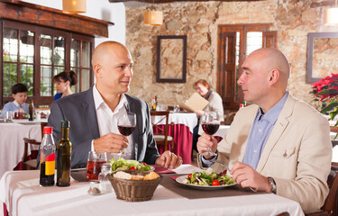 Portrait of two male friends drinking wine and eating salad at restaurant