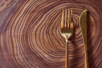 The golden fork and knife lies on a slice of a tree. wooden table. With copy space.
