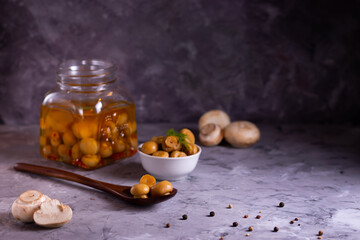 Fermented canned champignon mushrooms in a wooden eco spoon and in a glass jar with garlic, bay...