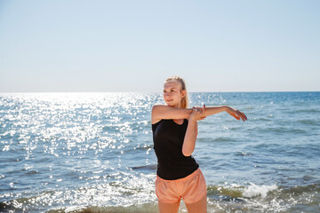 A blonde girl in a dark t shirt and light shorts does sports in the summer on the sea coast