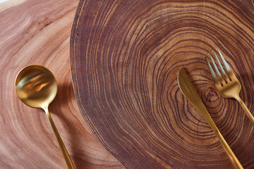 The golden spoon, knife and fork lies on a slice of a tree. wooden table. With copy space.