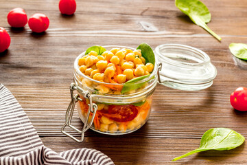 Vegan lunch. Chickpeas, carrot, tomato in glass jar on wooden table