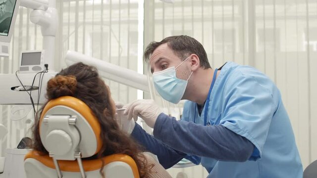 Rear view of Caucasian woman lying on dental chair while male prosthodontist checking result of his work. Then they discussing x-ray image on screen