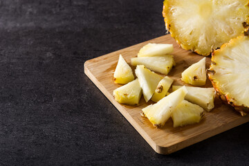 Fresh pineapple slices on cutting board and black stone background. Copy space	