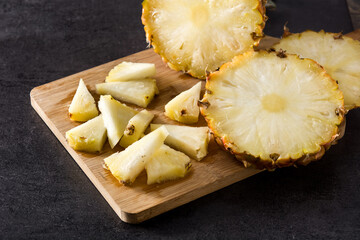 Fresh pineapple slices on cutting board and black stone background	