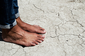 bare feet of a man on a cracked dry soil