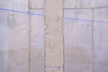 A concrete pillar in the center of the image, with the unfocused background of a cement wall with a blue line.