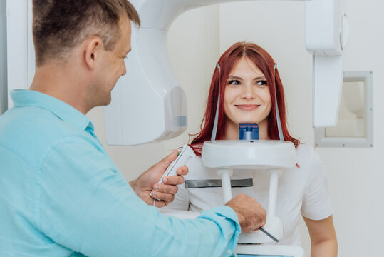 A girl patient makes a panoramic X-ray of the oral cavity on an orthopantomographic apparatus, and the dentist takes a picture