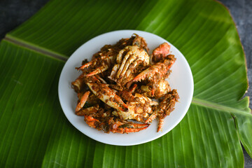 Chili crab curry or Kerala crab roast and rice, popular hot and spicy seafood dish in India, Sri Lanka, Singapore. Woman hand cooking roasted coconut sauce on dark background.