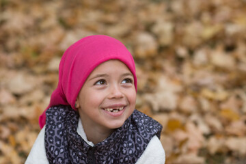 little girl in pink cap is smiling, mouth without teeth, girl portrait in autumn nature