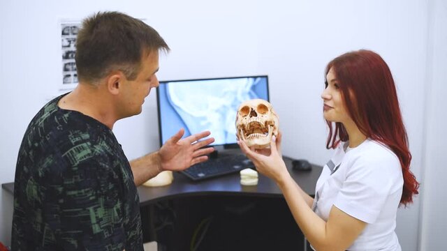 Doctor dentist teaches a student how to treat teeth using the example of a human skull