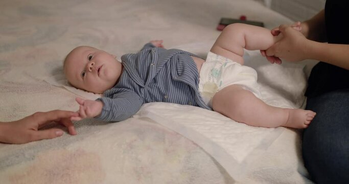 Little newborn baby lying on bed during massage of legs by physiotherapist