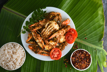 Chili crab curry or Kerala crab roast and rice, popular hot and spicy seafood dish in India, Sri Lanka, Singapore. Woman hand cooking roasted coconut sauce on dark background.