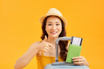 Portrait of young Asian woman with her passprt and luggage over orange background.