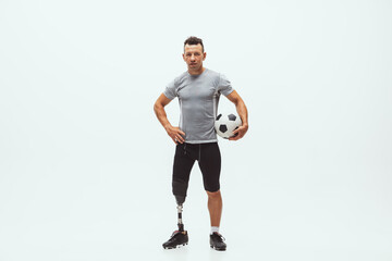 Athlete with disabilities or amputee on white studio background. Professional male football player with leg prosthesis training in studio. Disabled sport and healthy lifestyle concept. Achievements.