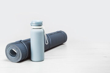 Rolled blue yoga mat and blue water bottle on grey wooden surface. Gender neutral fitness yoga and exercise concept with copy space. Active lifestyle and sport. Workout at home or gym banner