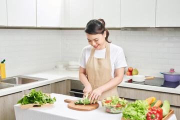 Young smiling housewife preparing healthy meal with vegetables in bright modern kitchen