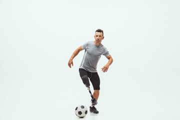 Fototapeta na wymiar Athlete with disabilities or amputee on white studio background. Professional male football player with leg prosthesis training in studio. Disabled sport and healthy lifestyle concept. Achievements.