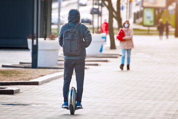 Man on mono wheel rolling on pavement. Electric unicycle. Guy driving on self balancing personal transporter with single wheel. Man with backpack on electric mono-wheel ride,  friendly city transport