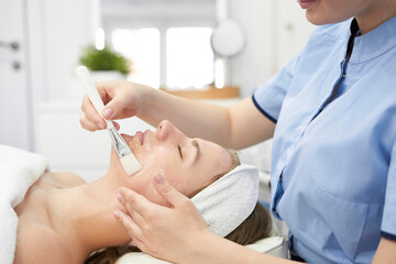 Obraz na płótnie Canvas Doctor cosmetologist makes a multi-stage facial cleansing procedure to a young attractive woman in a beauty salon. Summer skin care