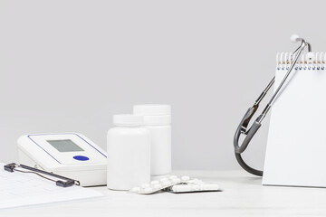 Medicine and pharmacy background. Pills and blood pressure monitor against monochrome grey background. Stethoscope. Mockup white vials. Medical concept. Copy space.