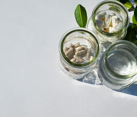 Glass jars with pills and water. Nearby are green leaves. Personalize natural healing. Copy space for text.