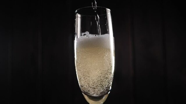 Close-up of the bartender pouring champagne into a glass on a black background, the glass has a lot of foam and bubbles. Slow motion.