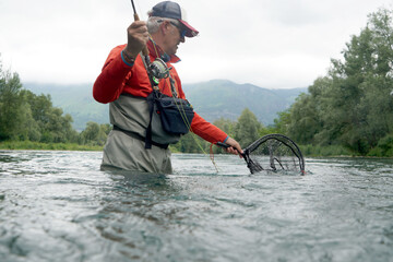 fly fisherman with a red backpack and a red jacket fishing in a high mountain river in summer
