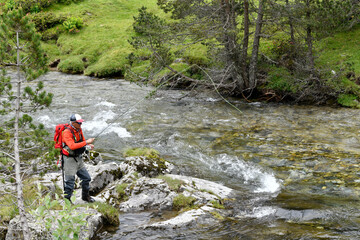 Fototapeta premium fly fisherman trout fishing with a hiking backpack and an orange jacket in the high mountains in summer