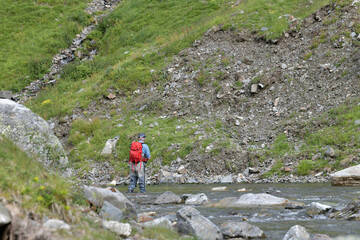 fly fisherman trout fishing with a hiking backpack and a blue shirt in the high mountains in summer