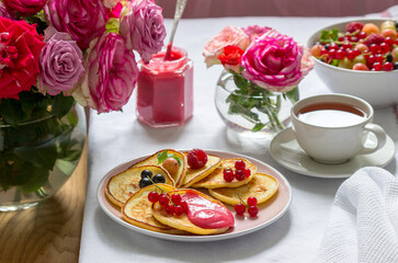 Curd pancakes with berry curd served with tea on a table decorated with bouquets of roses.