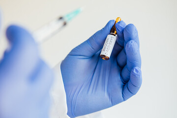 Doctor holds a syringe with a needle in one hand and a container with the COVID-19 vaccine in the...