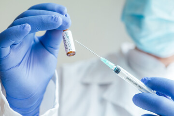 Doctor holds a syringe with a needle in one hand and a container with the COVID-19 vaccine in the...