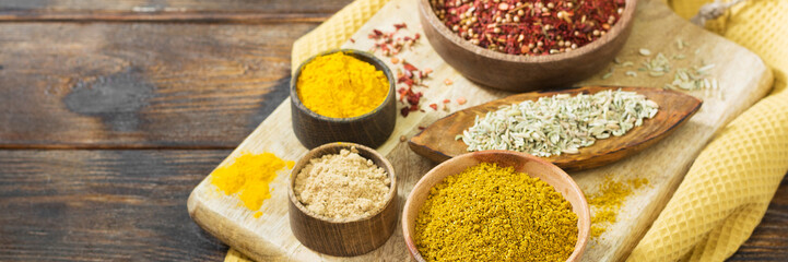 Spices and seasonings in wooden bowls on a brown wooden table. Spices close-up with space for text. The view from the top. Banner