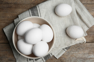 Many fresh raw chicken eggs in bowl on wooden table, flat lay