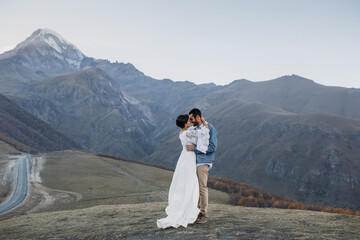 Young Georgian couple posing in the mountains. Boho wedding in Georgia. Evening setting sun. Blue jeans jacket