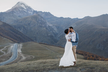 Young Georgian couple posing in the mountains. Boho wedding in Georgia. Evening setting sun. Blue jeans jacket