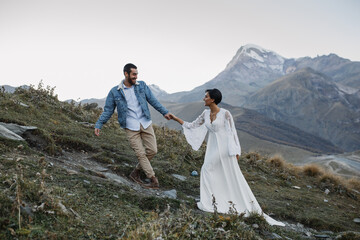 Young Georgian couple posing in the mountains. Boho wedding in Georgia. Evening setting sun. Blue jeans jacket