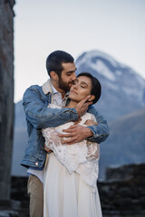 Young Georgian couple posing in the mountains. Boho wedding in Georgia. Evening setting sun. Blue jeans jacket
