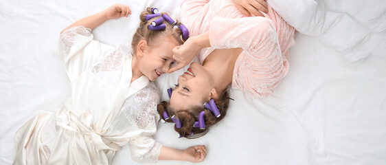 Happy mother and daughter with curlers lying on bed, top view. Banner design