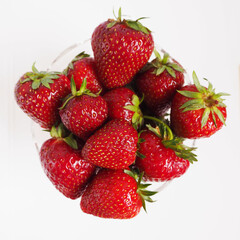 red ripe strawberries in a transparent glass plate top view on a light gray background