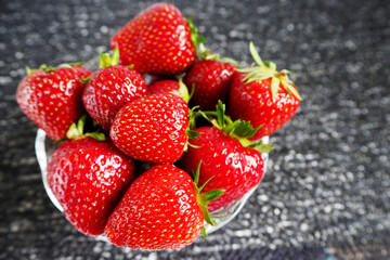 red ripe strawberries in a transparent glass plate top view on a black textured background
