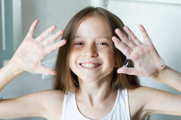 Happy smiling girl washing hands, show hands in soap bubbles to the camera.