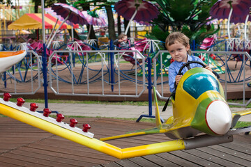 The boy is sitting on the plane. The kid rides on an amusement ride. Happy childhood of a boy in an...