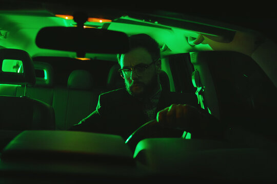 Businessman In Glasses Sitting At Night In The Car In The Green Light.