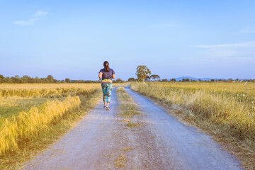 Fototapeta na wymiar Back view of woman running and exercising on the path through the rice fields in the evening.