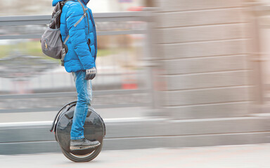 Man riding fast on electric unicycle on city street. Mobile portable individual transportation vehicle. Personal vehicle for transportation. Boy with backpack on electric mono-wheel (EUC) © Tricky Shark